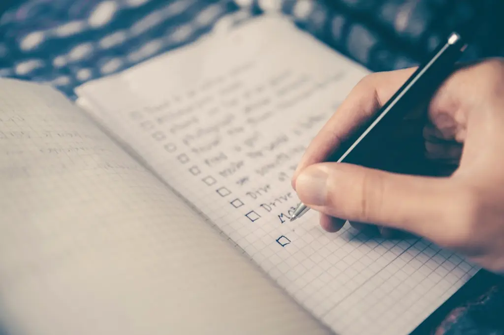 A hand checking off items on a handwritten checklist in a notebook
